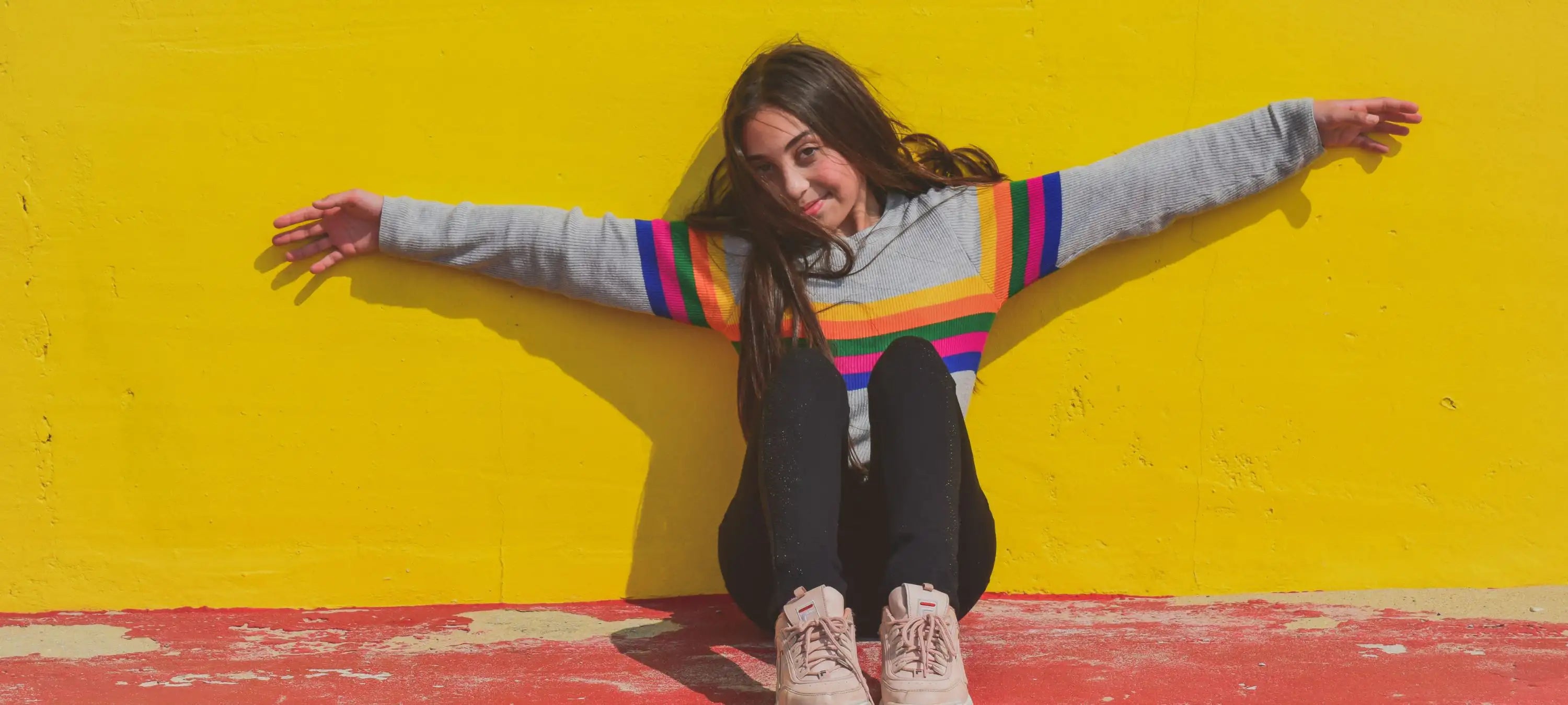 Ein Teenagermädchen breiten die Arme vor einer gelben Wand aus.