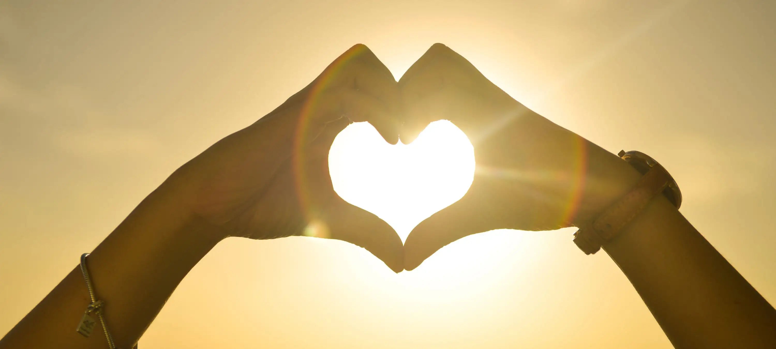 Sonnenlicht scheint durch zwei Herz formende Hände.