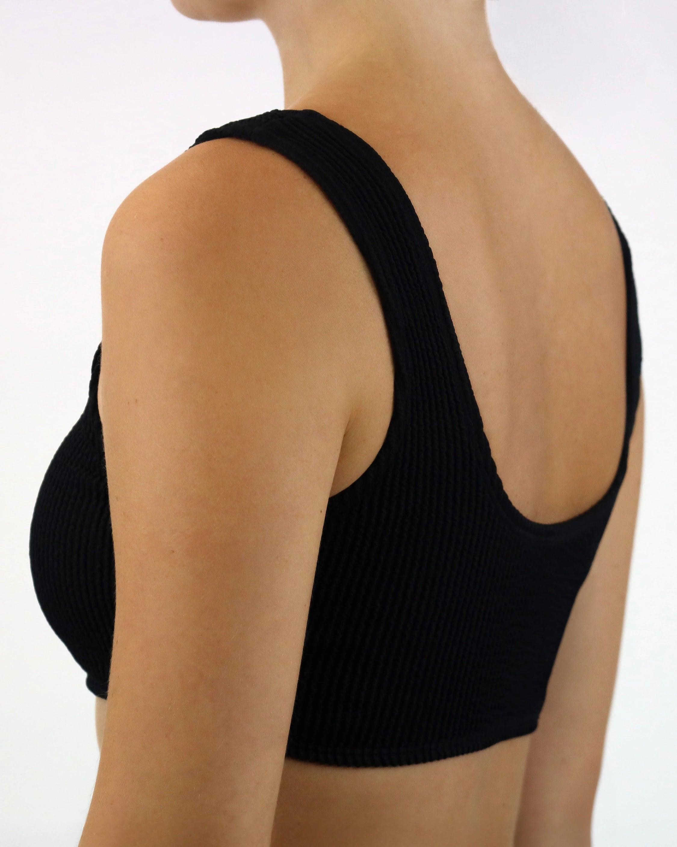 Schwarzes geripptes Bikini-Oberteil mit tiefem Rückenausschnitt und breiten Trägern, aus weichem, elastischem Material für maximalen Komfort.