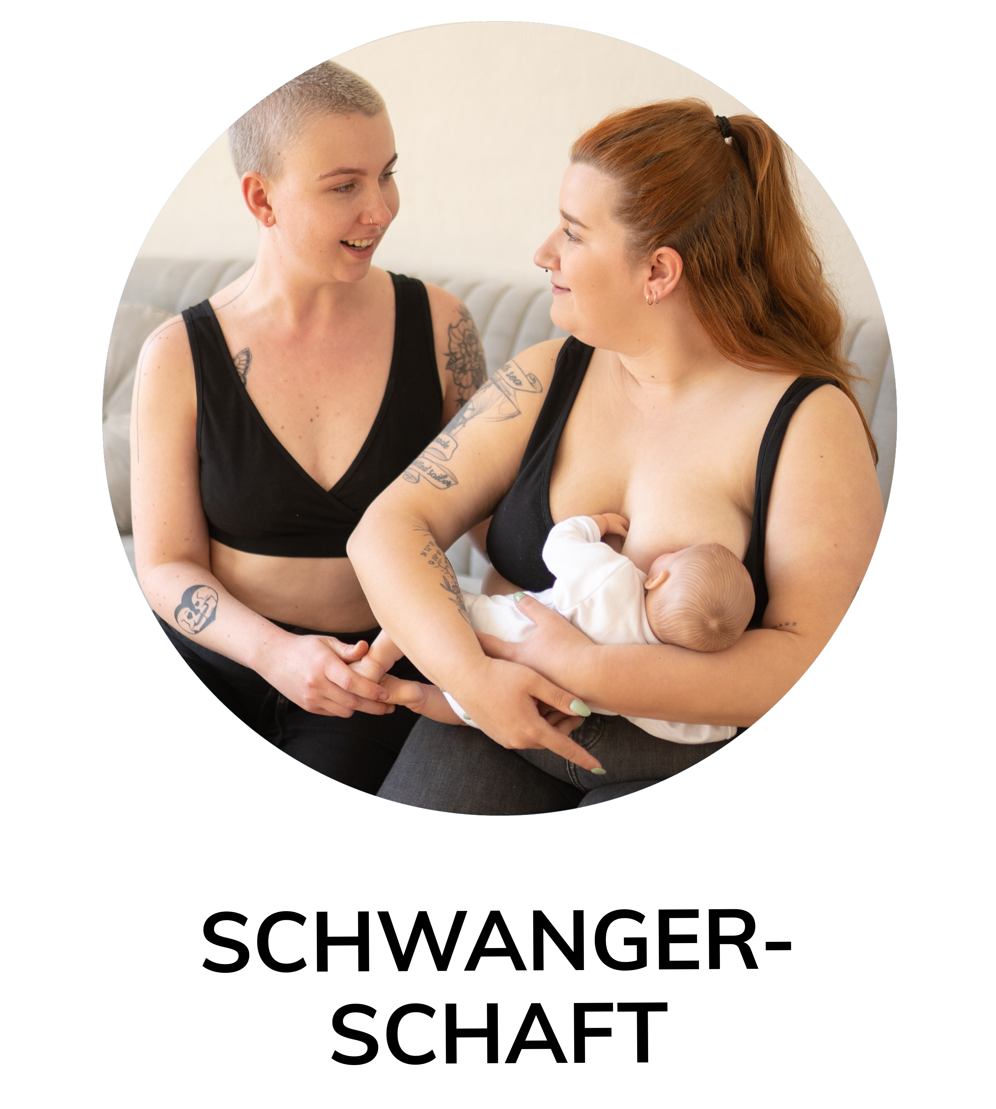 Zwei Frauen in Still-BHs, eine stillt ein Baby, die andere hält ihre Hand, beide lächeln auf dem Sofa.