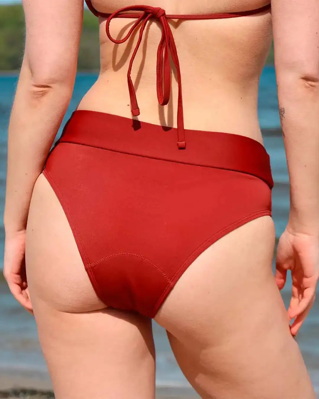 Frau in roter Bikini Hose steht mit dem Rücken zur Kamera und schau aufs Meer raus.