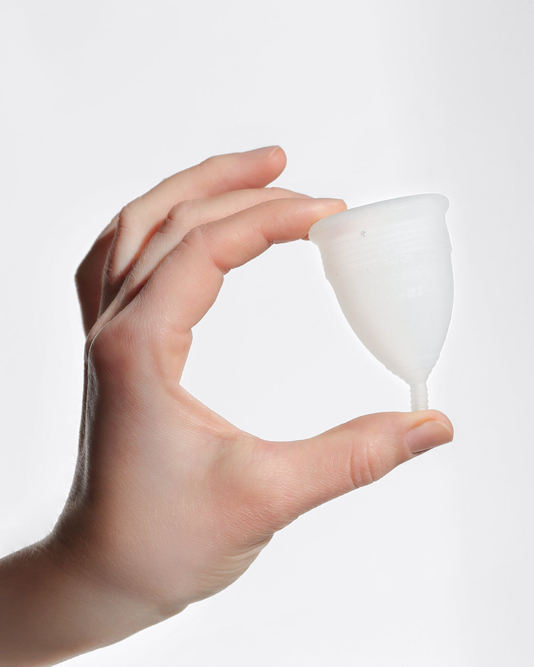 and hält eine weiße MYLILY Menstruationstasse aus weichem, medizinischem Silikon – nachhaltige und wiederverwendbare Alternative zu Tampons."