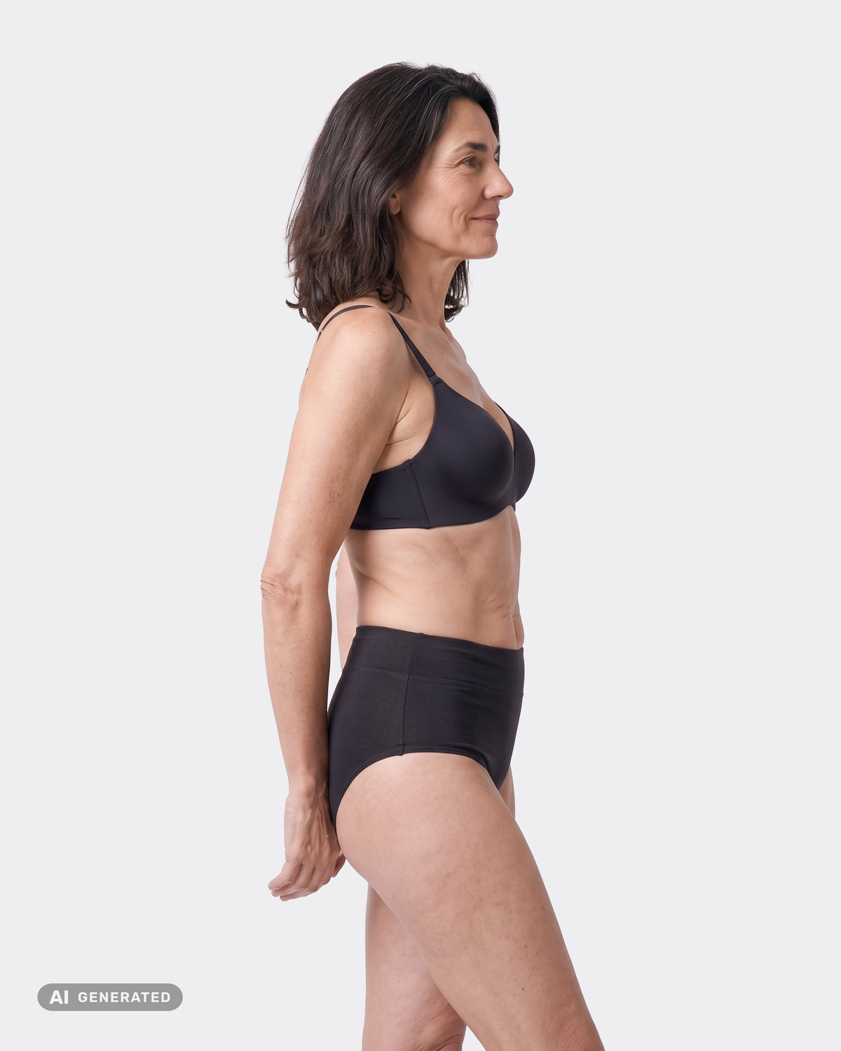 Frau im Profil in schwarzem High-Waist-Periodenslip und BH, die Hände hinter dem Rücken.