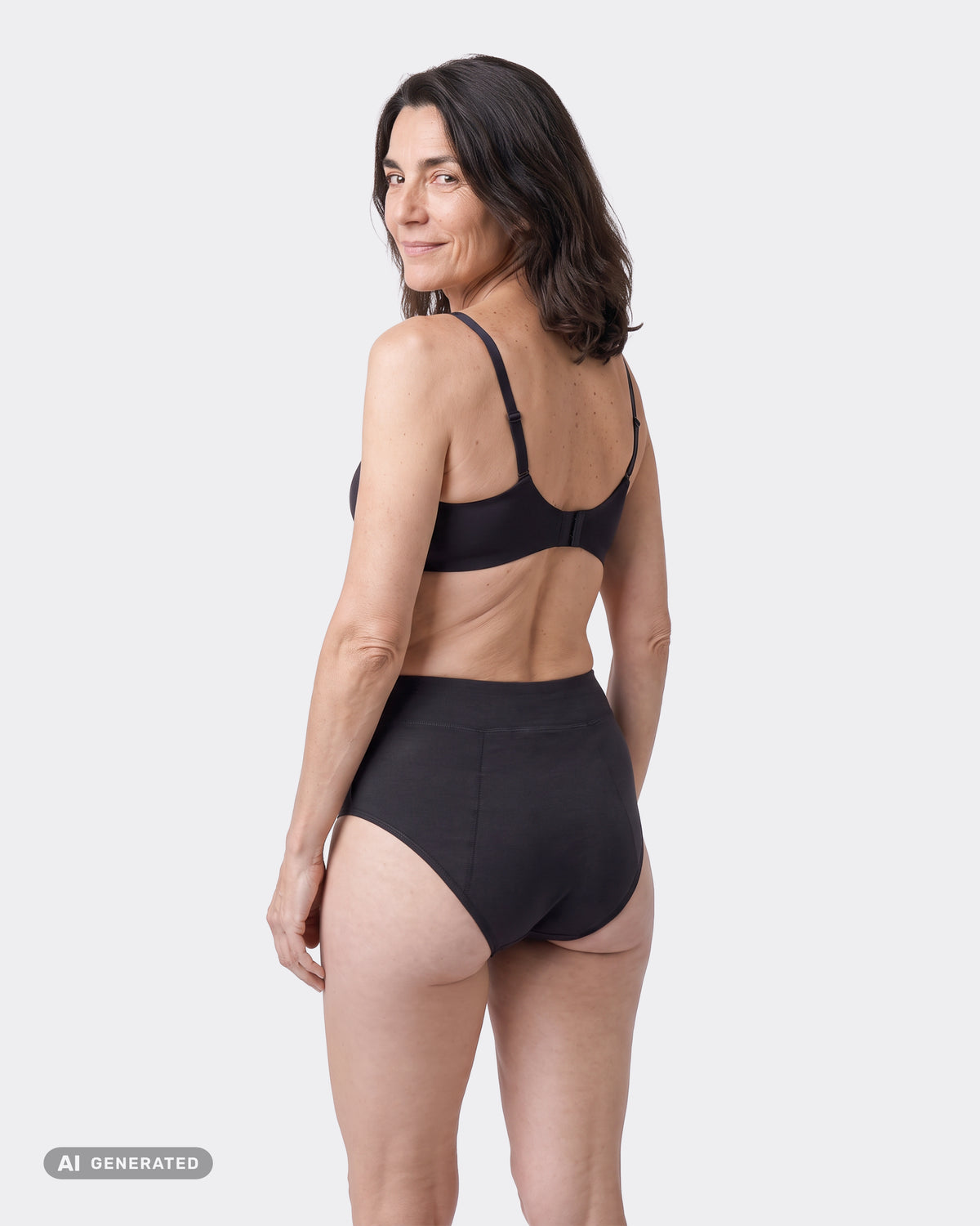 Frau in schwarzem High-Waist-Periodenslip und BH von hinten, sie blickt lächelnd über die Schulter.