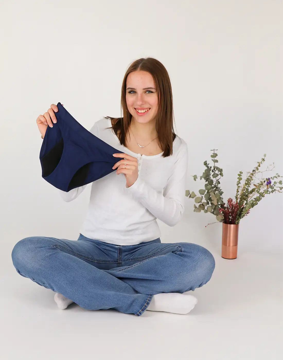 Ein Mädchen sitzt im Schneidersitz auf dem Boden und hält eine Periodenunterwäsche für Teenager in der Hand.