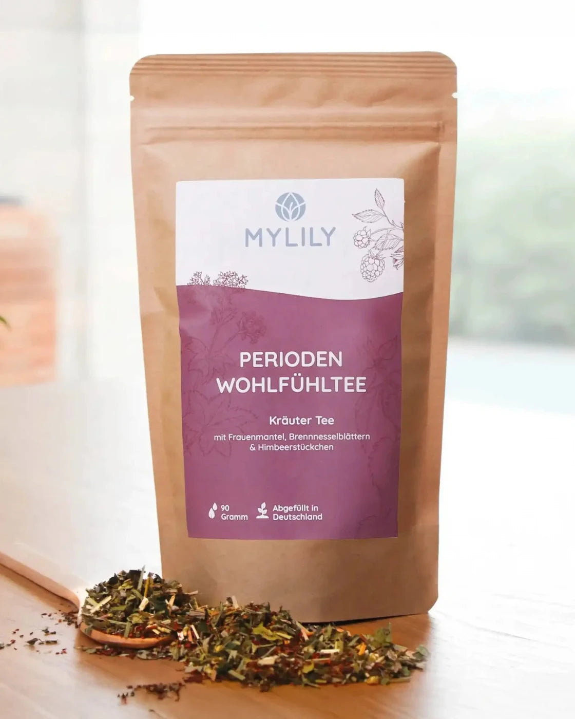 Löffel mit loser Kräuterteemischung vor Packung Kräuterteemischung Perioden Wohlfühltee