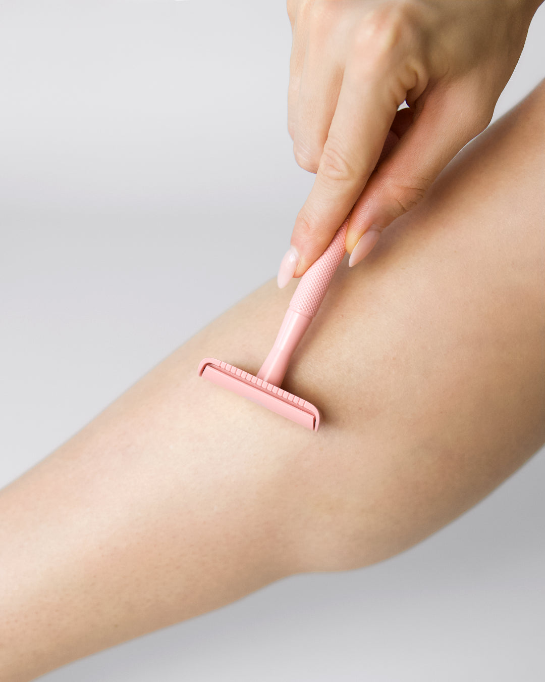 Hand hält einen rosa Rasierer und rasiert damit ein Bein auf heller Haut.