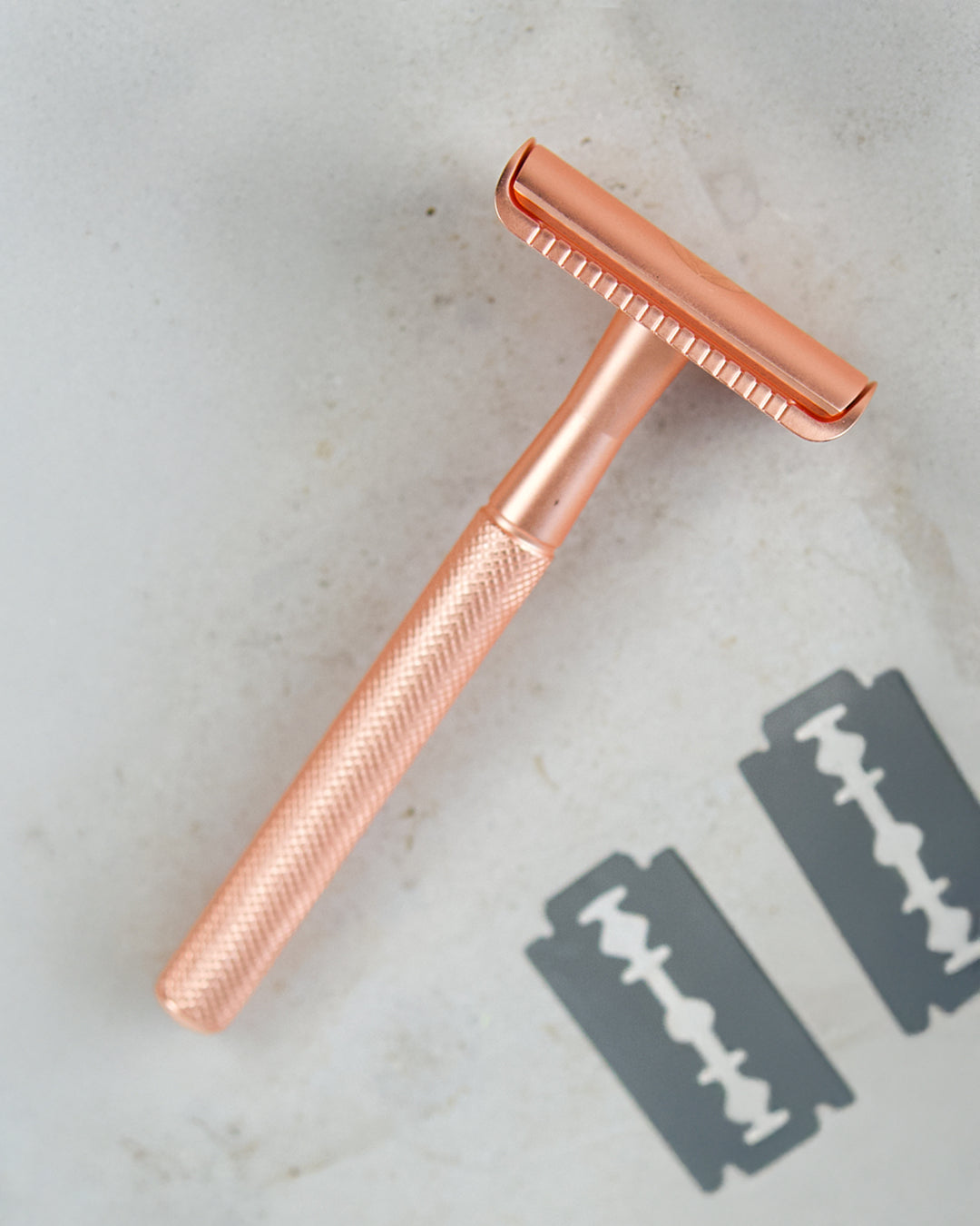 Rosegoldener Rasierer mit strukturierter Griffoberfläche auf grauem Hintergrund.