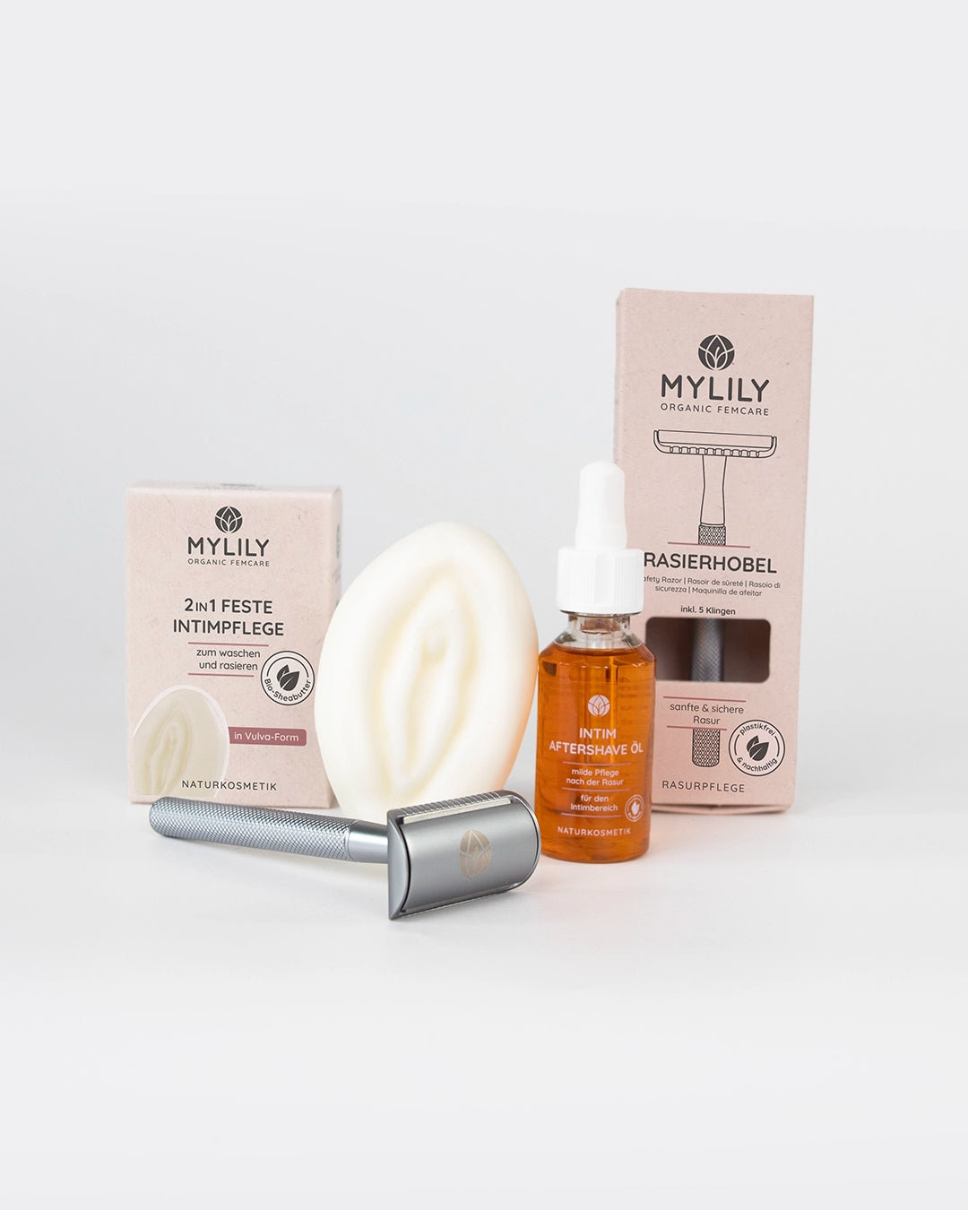 Das Vulva Care Set Produkte aufgereiht mit Rasierhobel, Aftershave Öl und Vulva Waschstück.