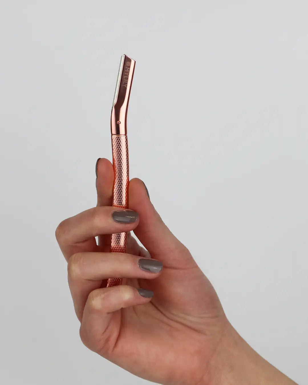 Augenbrauenrasierer in Roségold in der Hand liegend. Er eignet sich, um Gesichtshaare zu entfernen.