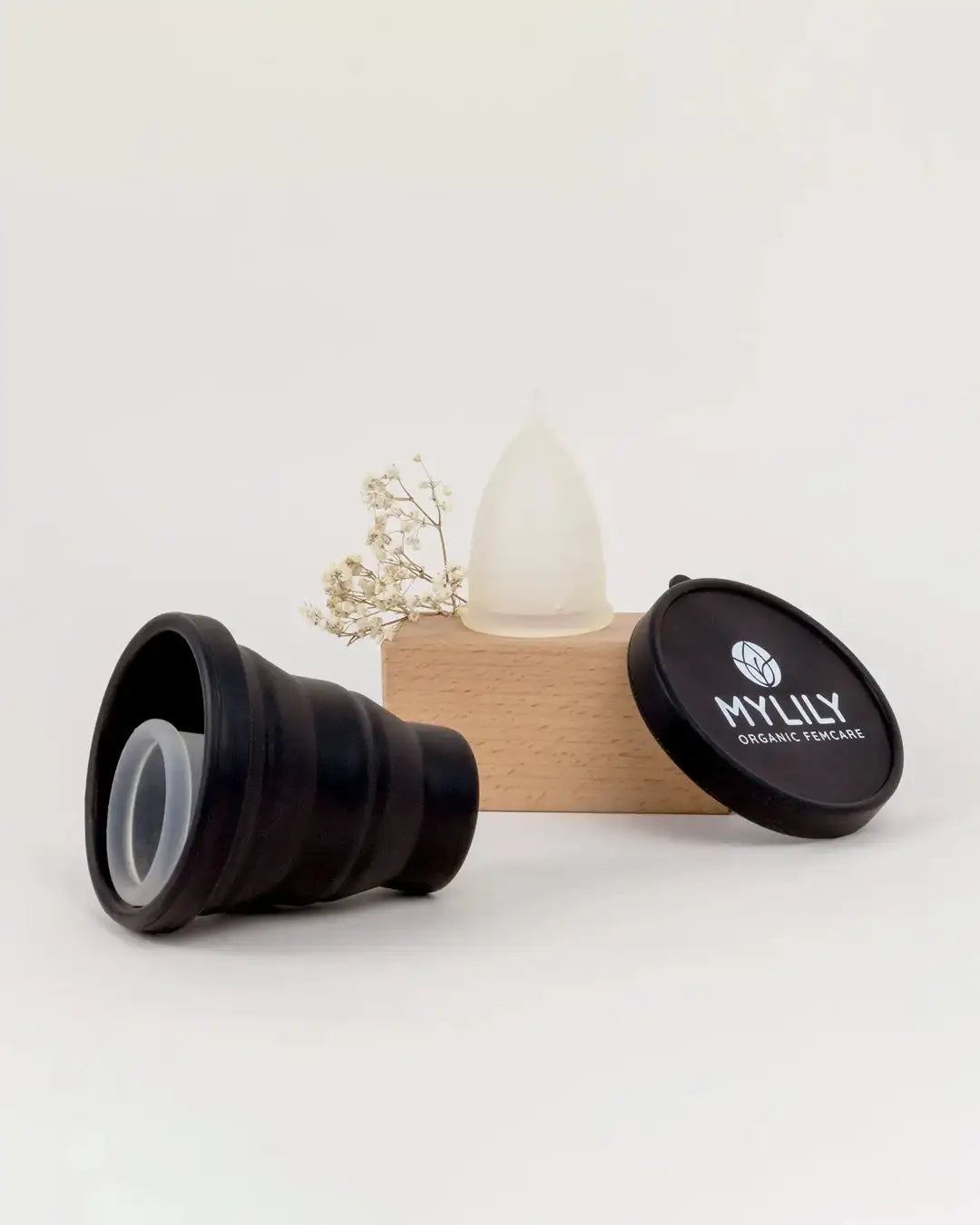 Menstruationstasse und schwarzes Reinigungscase vor Holzblock mit Blume