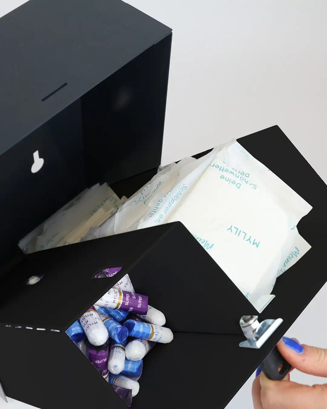 Der schwarze Tamponspender von MYLILY geöffnet und befüllt mit Binden und Tampons