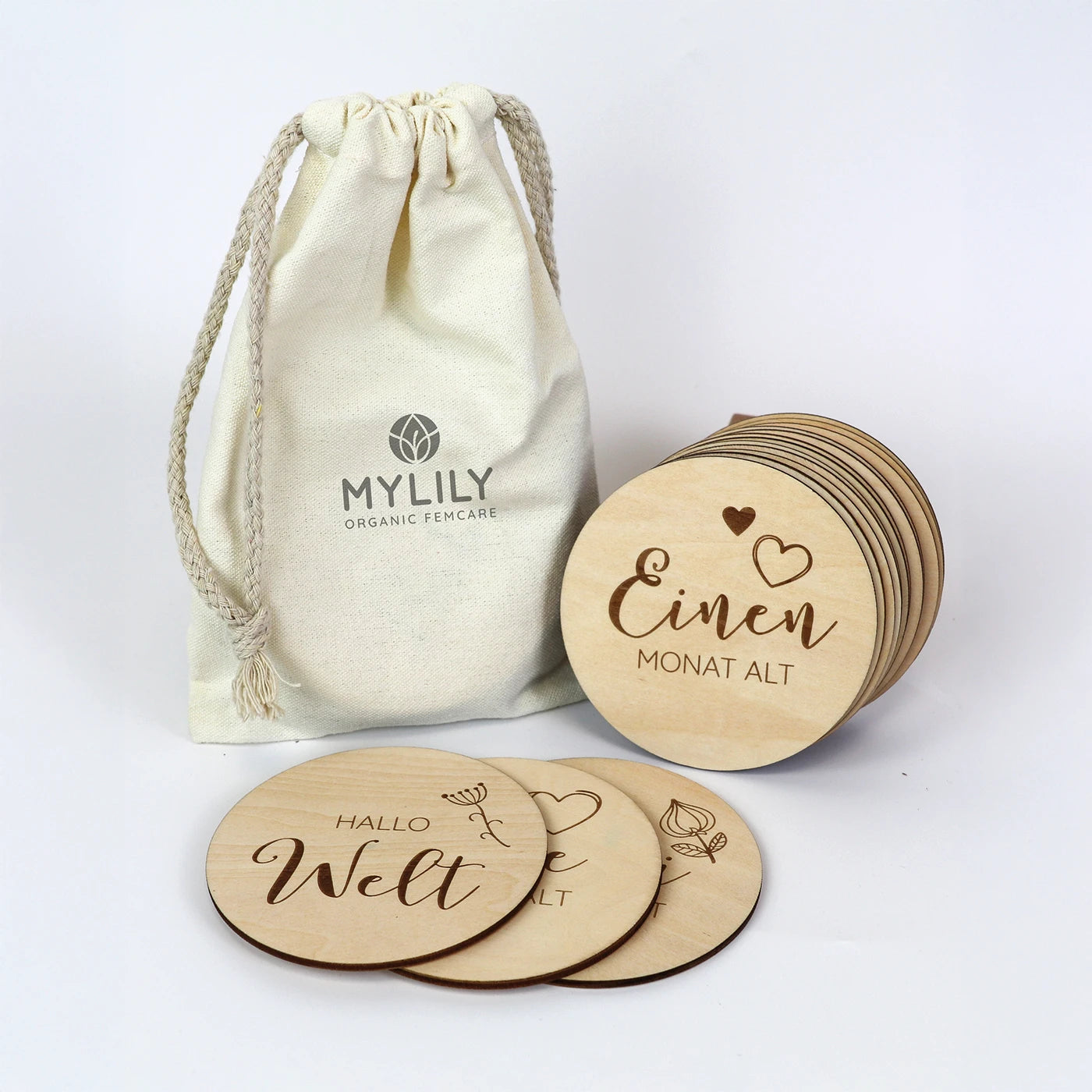 Runde Meilensteine aus Holz für die Entwicklung des Babys im ersten Lebensjahr neben cremefarbenen Baumwollsäckchen von MYLILY