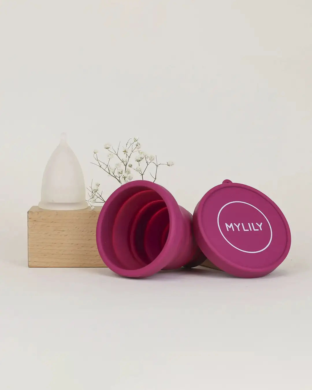 Menstruationstasse und beerenfarbenes MYLILY Reinigungscase vor Holzblock mit Blume
