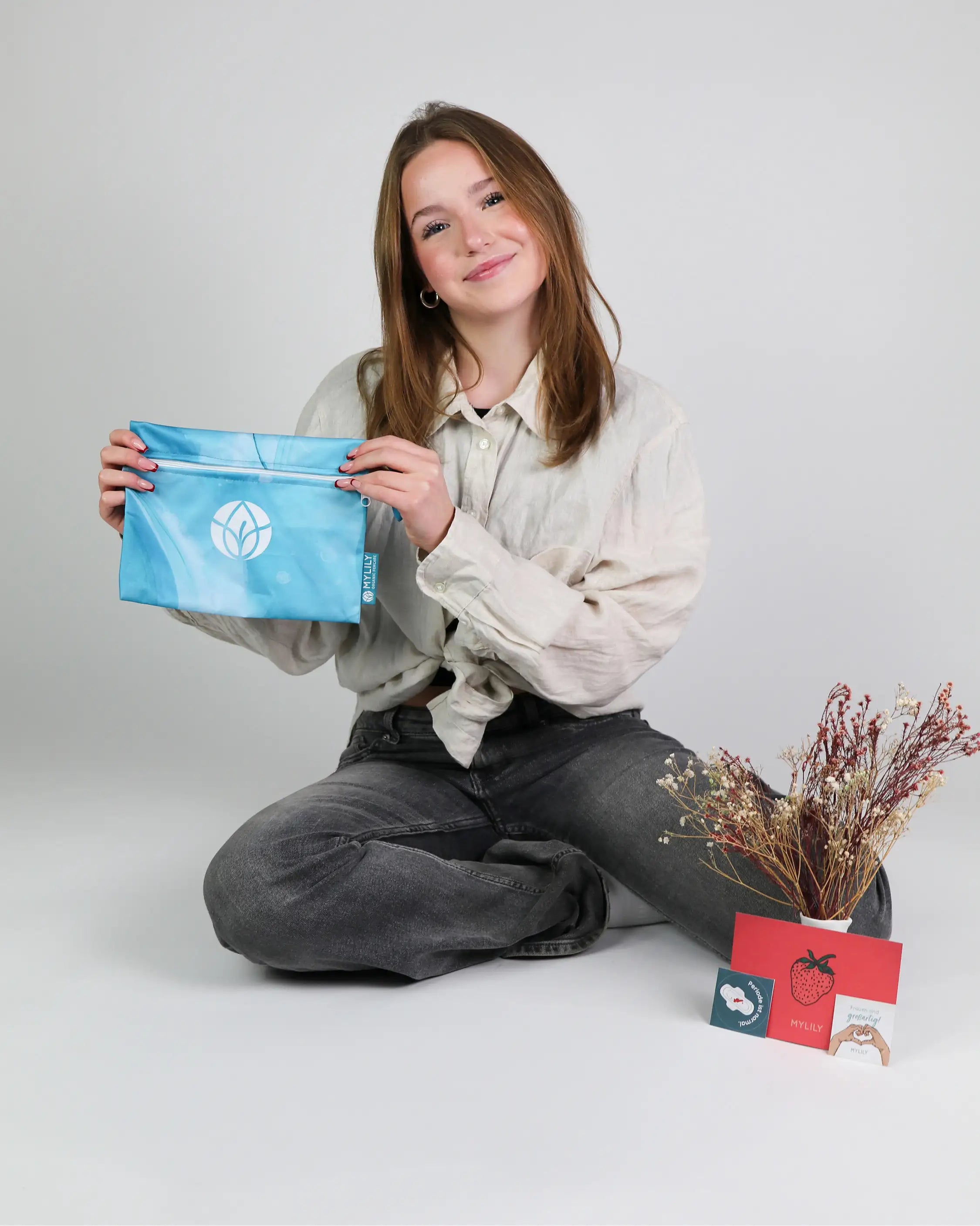 Mädchen hält blaue Wetbag in den Händen vor Postkarte, Sticker und Trockenblumen