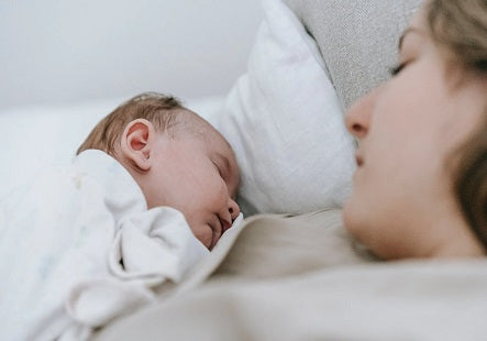 Eine Frau liegt mit einem Baby auf der Brust im Bett. Im Wochenbett sollen sich Mama und Kind kennenlernen und gemeinsam erholen