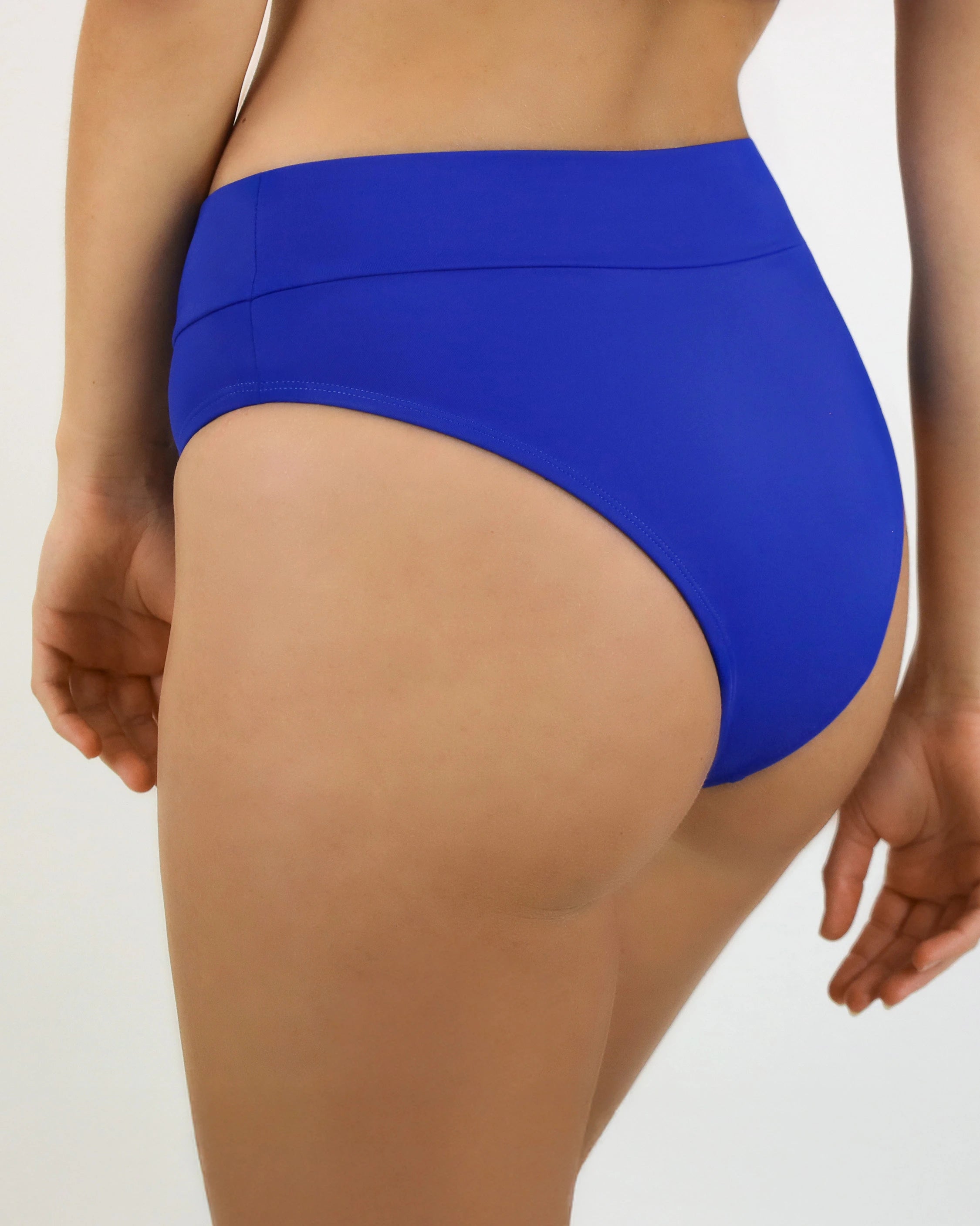 Model steht dynamisch vor weißer Leinwand und trägt die Bikinihose Basic Slip in royalblau.