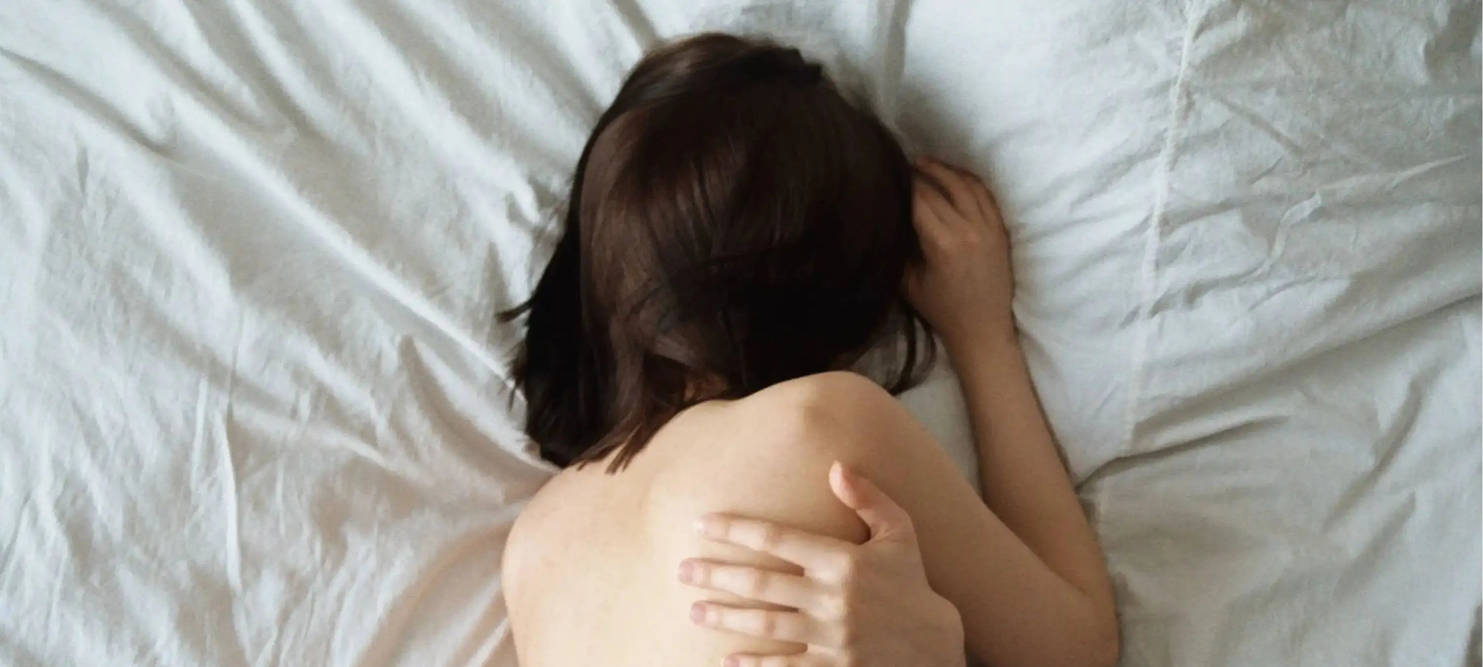 Eine Frau verkrampft vor Schmerzen im Bett und liegt seitlich auf dem Baauch.