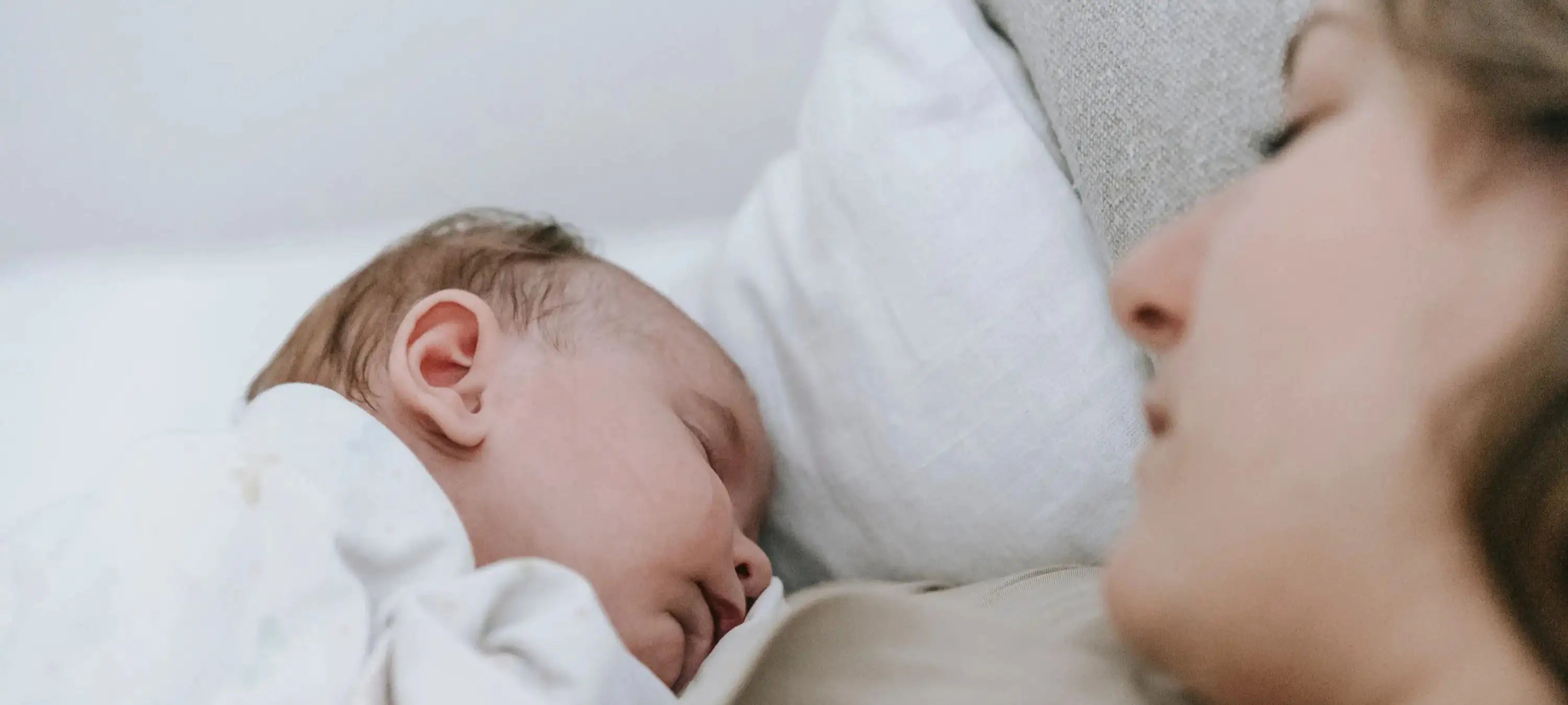 Ein Baby liegt neben seiner Mutter im Bett und schläft.