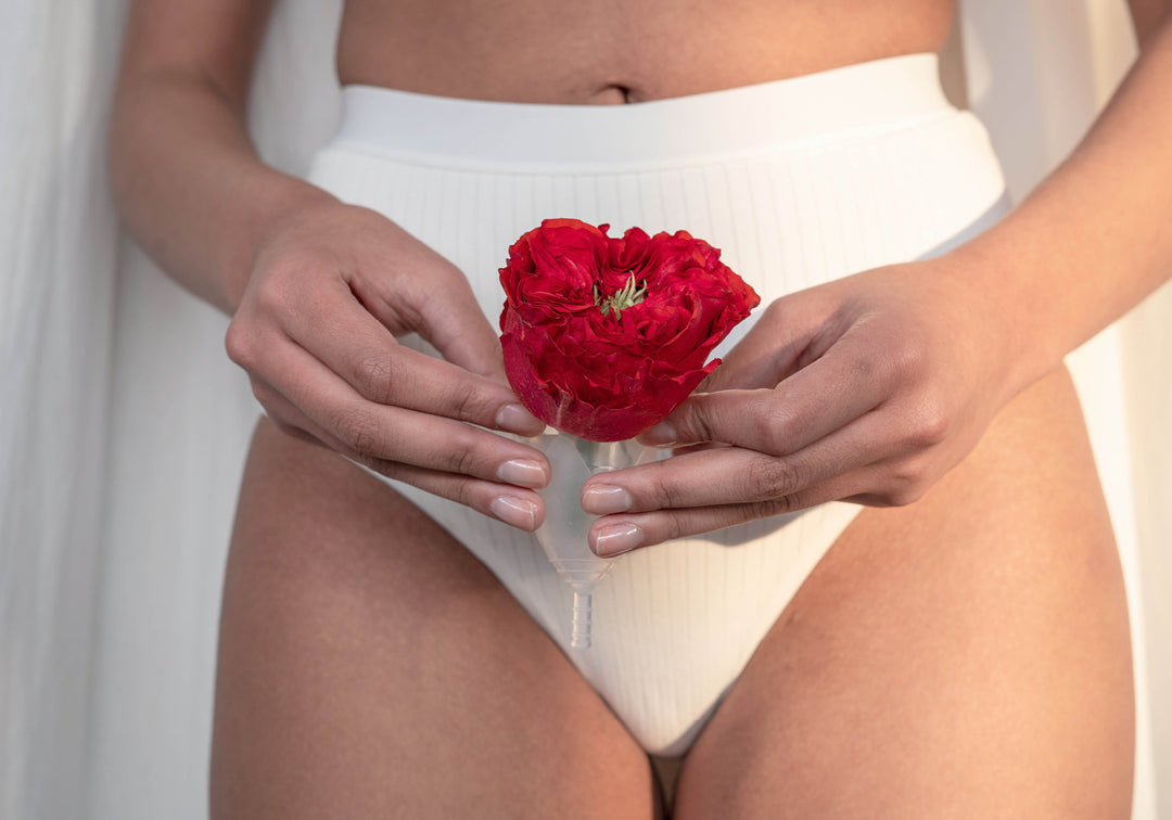 Eine frau hält eine rote Blume vor ihren Intimbereich. Aufklärung und Tipps zum Thema Manstruation, Periodenprodukte, Verhütung und vieles mehr