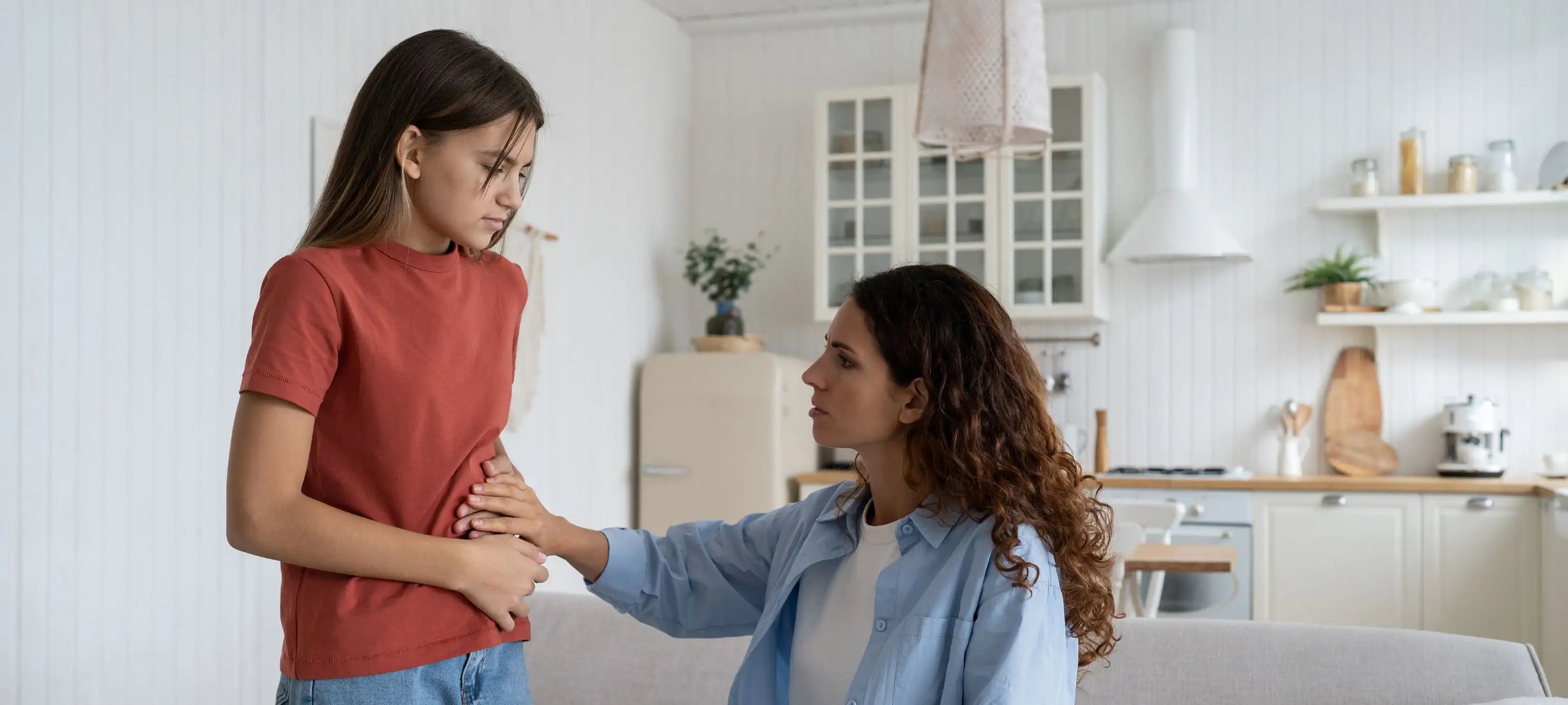 Eine Mutter legt besorgt ihre Hand auf den Bauch der Tochter.