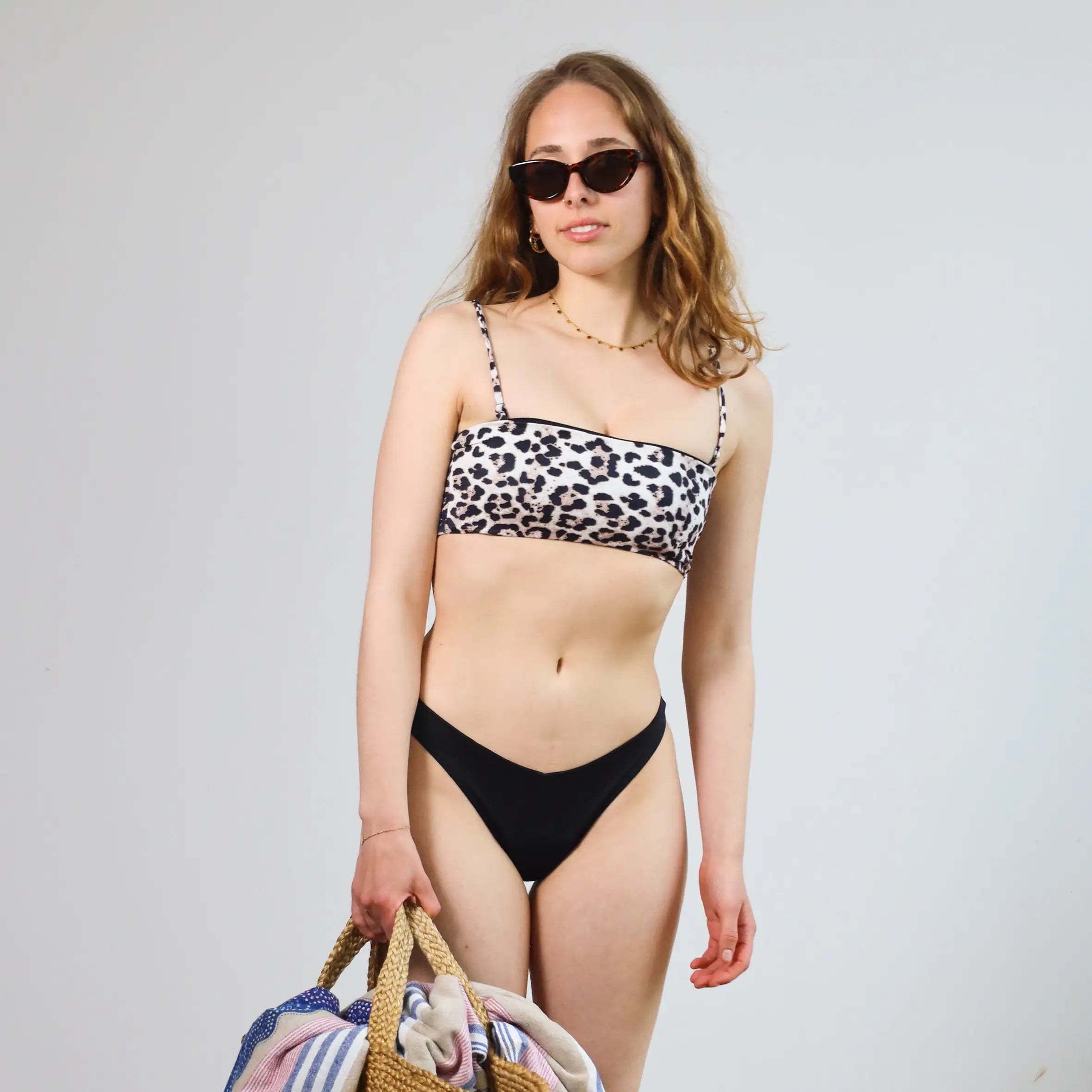 Frau mit Sonnenbrille und goldener Kette in einem Leo Bikini trägt eine Strandtasche. #farbe_leo