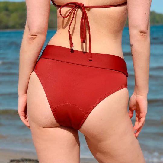 Frau in roter Bikini Hose steht mit dem Rücken zur Kamera und schau aufs Meer raus. #farbe_hagebutte