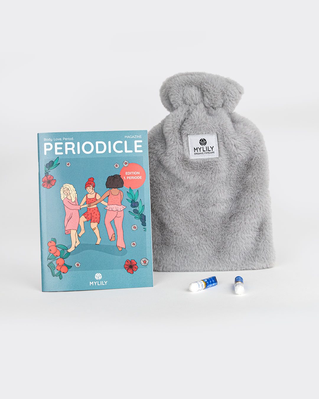 MyLily Periodicle Magazin neben grauer Plüsch-Wärmflasche und zwei Mini-Tampons