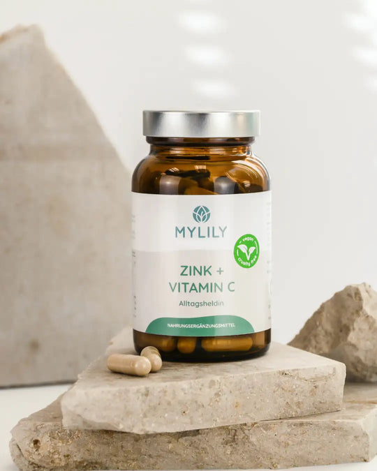 Vitamin C und Zink Kapseln von MYLILY in einer umweltfreundlichen Glasflasche auf Steinplatten platziert.