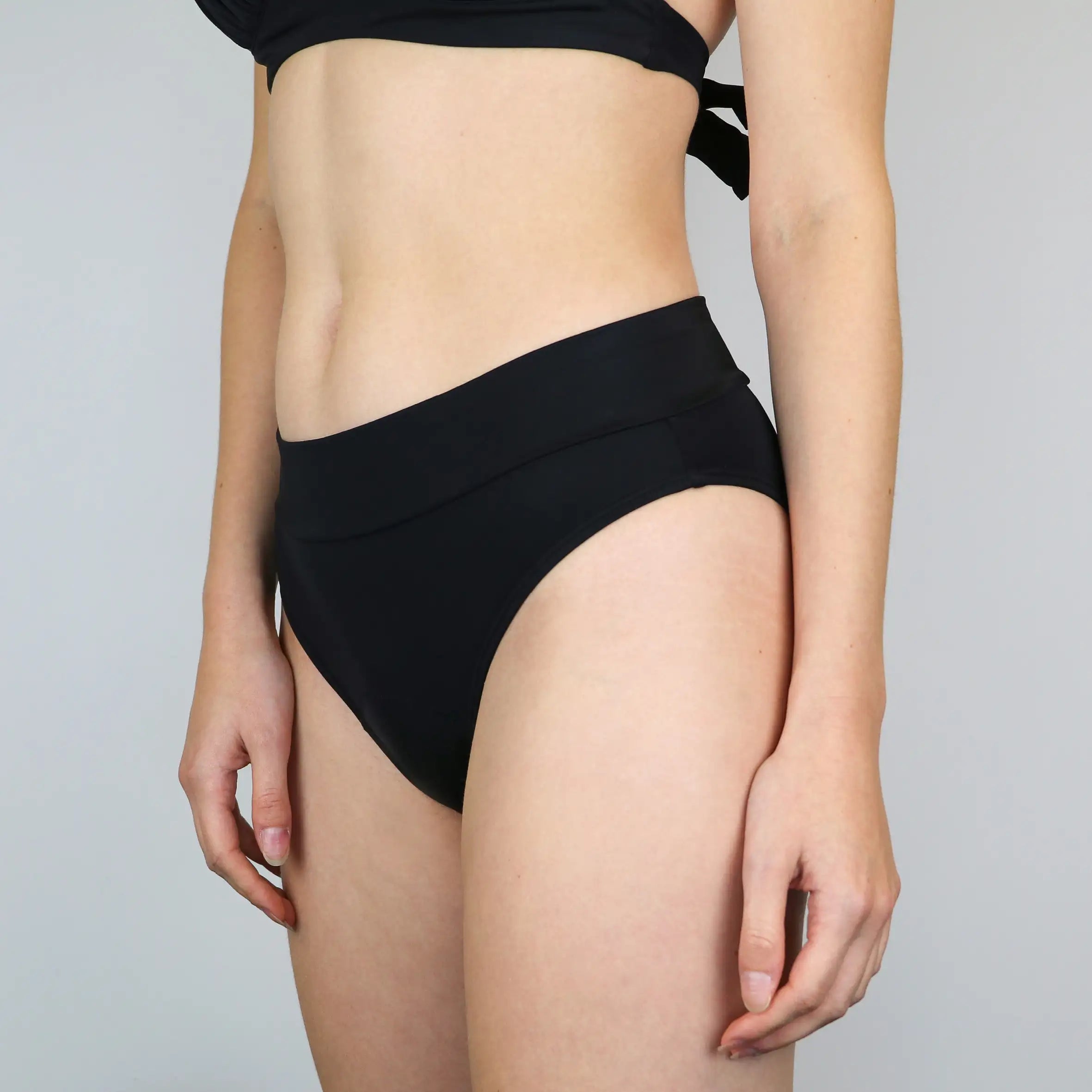 MYLILY Bikinihose Basic Slip schräg von der Seite. Perioden Bademode. Vegan und nachhaltig MYLILY organic femcare aus Bio-Baumwolle. Für die Periode von Frauen der perfekte Perioden Bikini.  #farbe_schwarz