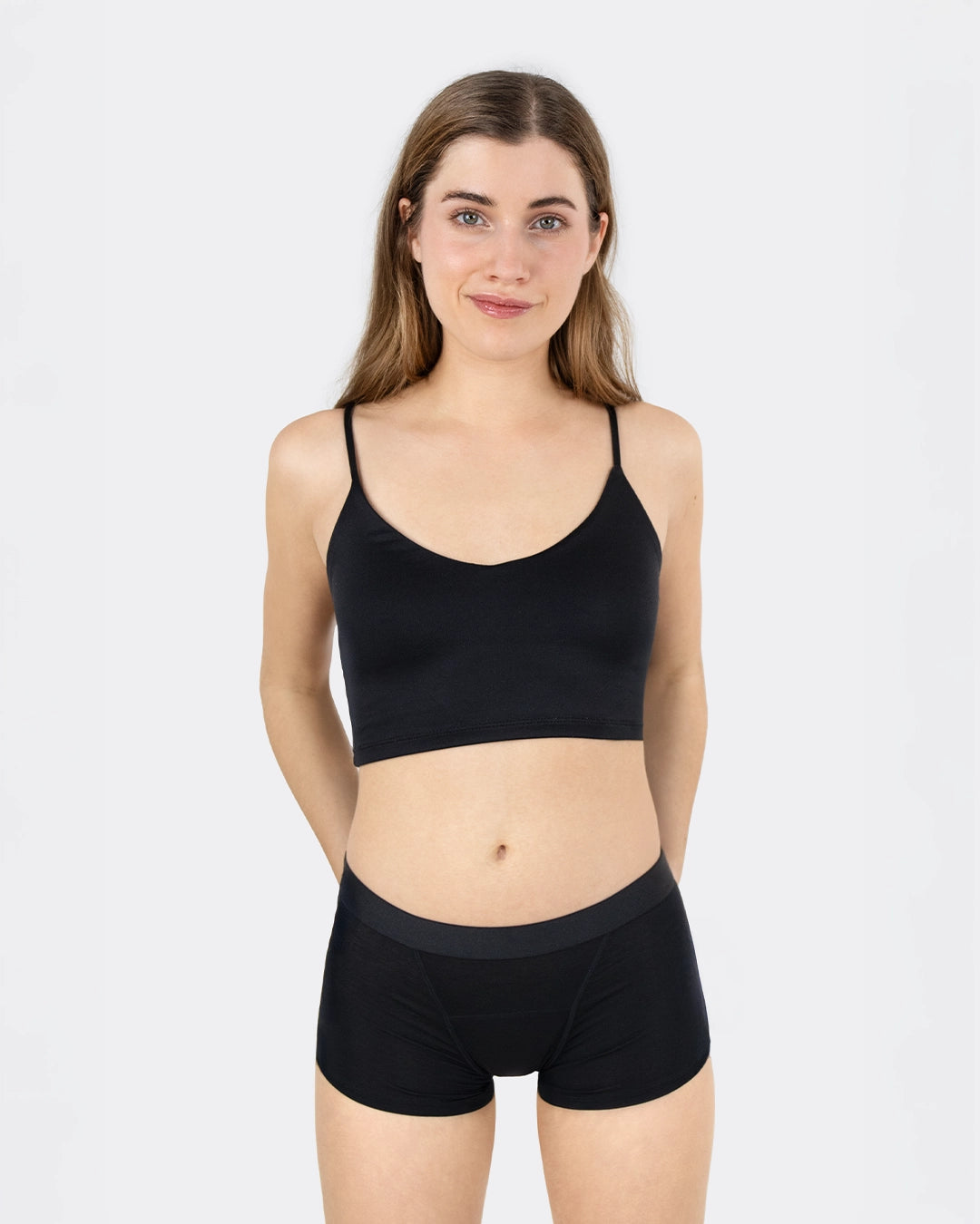Junge Frau trägt einen schwarzen Periodenslip im Boxer-Schnitt mit breitem Bund und ein schwarzes Bustier.