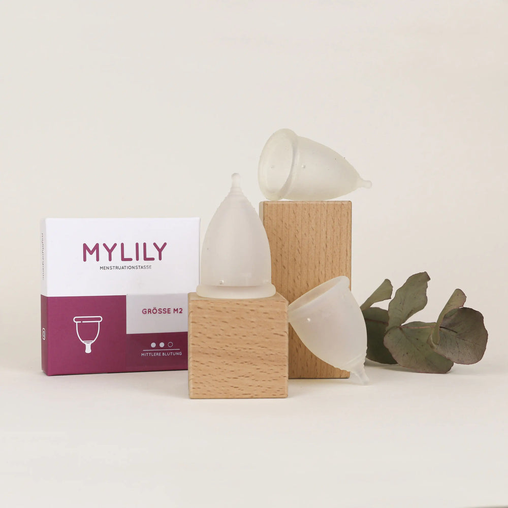 Die verschiedenen Größen der Menstruationstasse mit Verpackung auf einem Holzblock