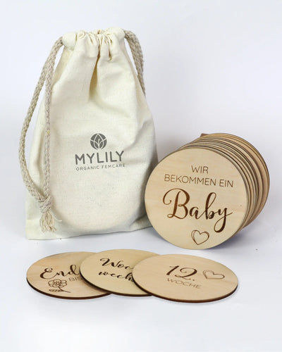 Ein Baumwollbeutel mit "MYLILY Organic Femcare" und runden Holzmeilensteinen mit Schwangerschafts-Gravuren.