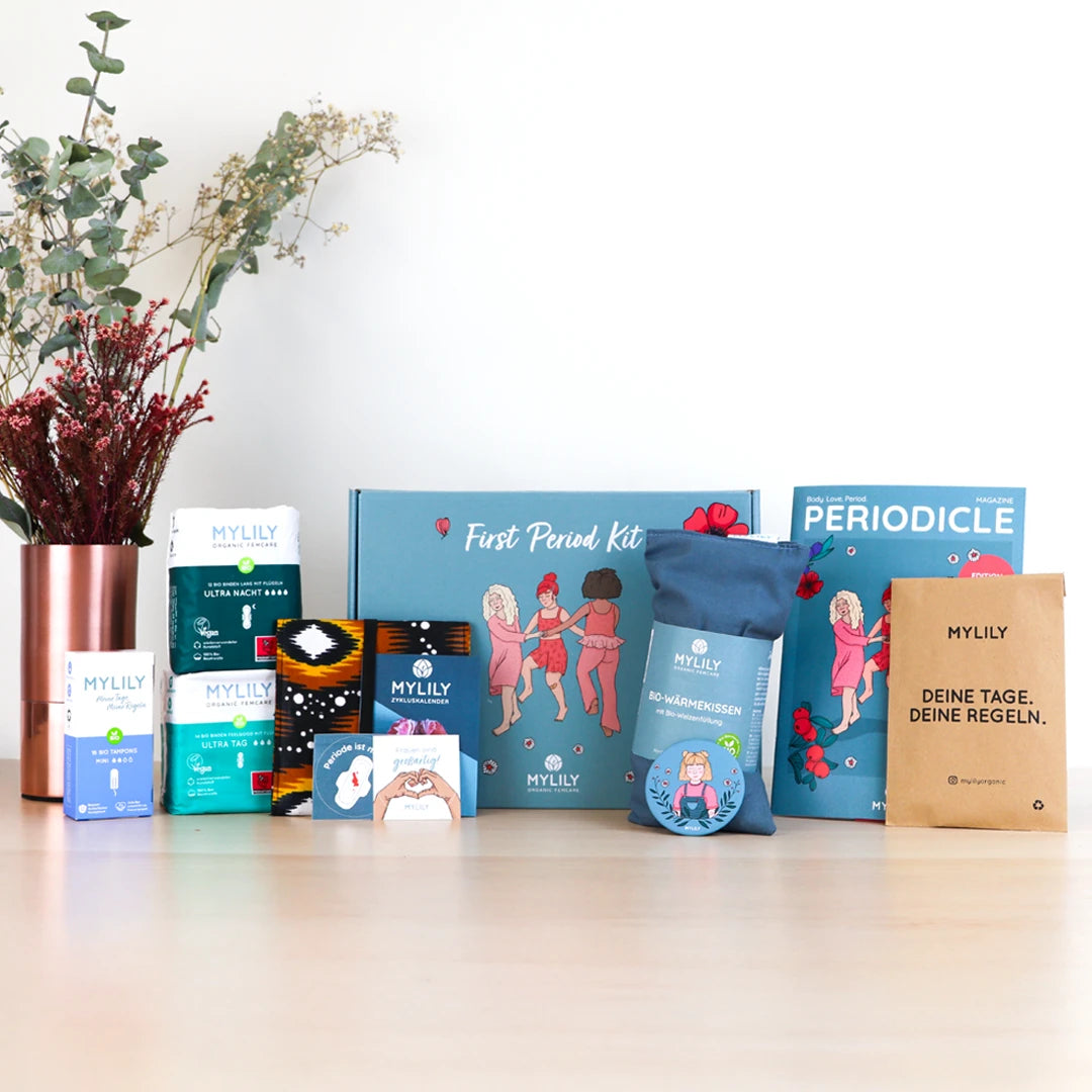 Inhalt des First Period Kits von MYLILY: Bio-Tampons, Bio-Binden, Bio-Slipeinalgen, Period Bag, Wärrmekissten, Aufklärungsmagazin aufgereiht vor Verpackungsbox